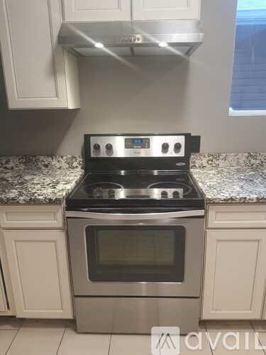 A stainless steel oven with a digital display is installed in a kitchen with white cabinets.