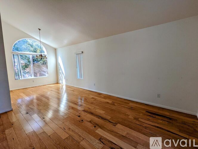 A spacious room with wooden flooring and a large window.