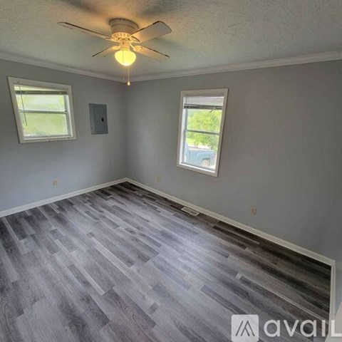 A room with a ceiling fan and two windows.