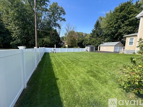 A white picket fence separates a lush green lawn from a residential area.