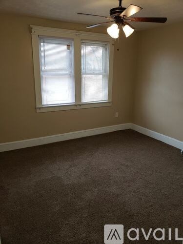 A room with a carpeted floor, a ceiling fan, and a window with blinds.