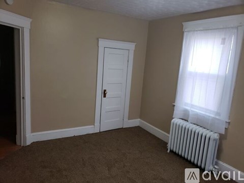 A room with a white door, a window with white curtains, and a white radiator.