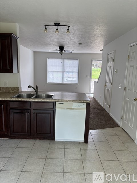A kitchen with a white dishwasher and dark brown cabinets.