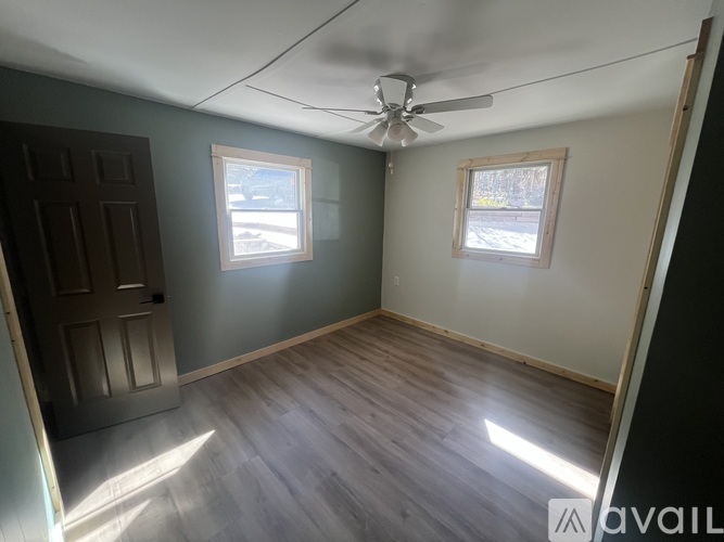 A room with a ceiling fan and two windows.