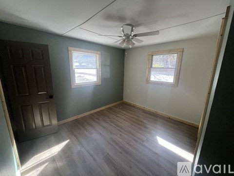 A room with a ceiling fan and two windows.