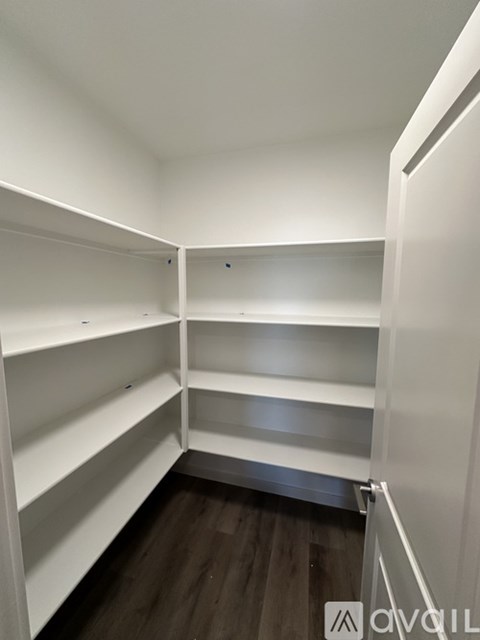 A white walk-in closet with shelves and a wooden floor.