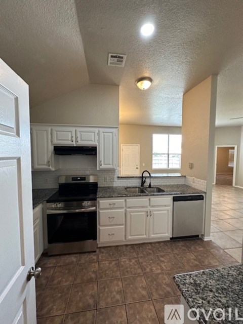 A kitchen with white cabinets and brown tiles.