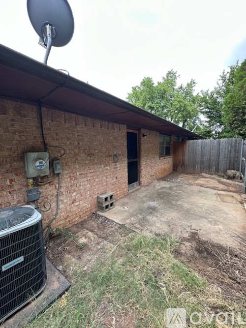 A backyard with a brick building, a satellite dish, and a heat pump.
