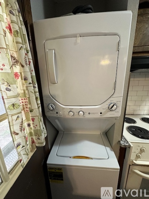 A white dishwasher is sitting in a kitchen next to a window with a curtain.