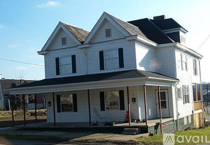 A white two-story house with a black roof and a porch.