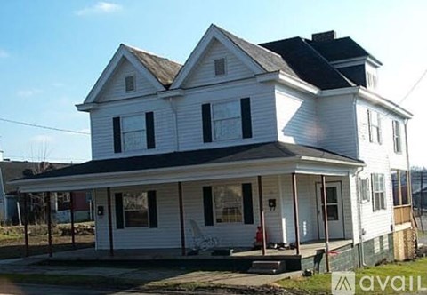 A white two-story house with a black roof and a porch.