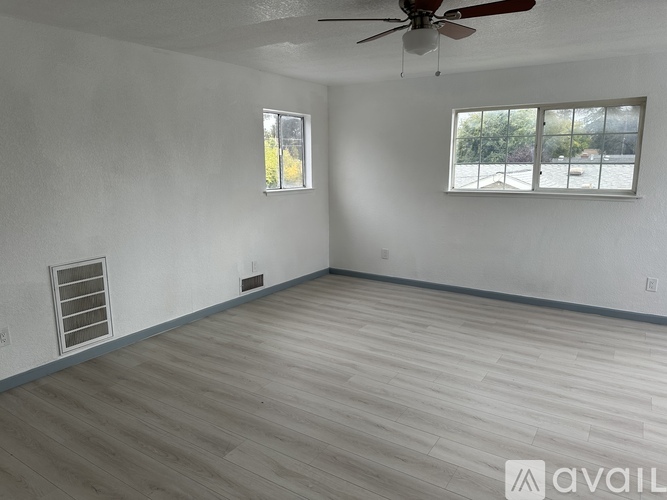 A room with a ceiling fan and two windows.