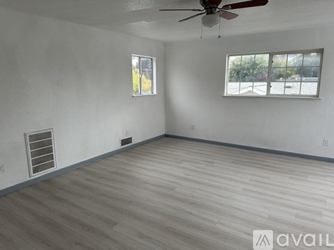 A room with a ceiling fan and two windows.