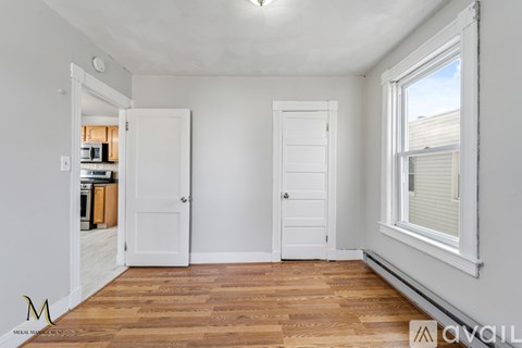 A room with wooden floors and white walls, with two doors and a window.
