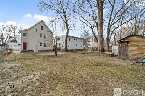 A large, two-story house with a red door is surrounded by bare trees and other buildings.