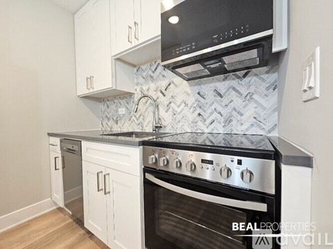 A modern kitchen with a black stove top oven and white cabinets.