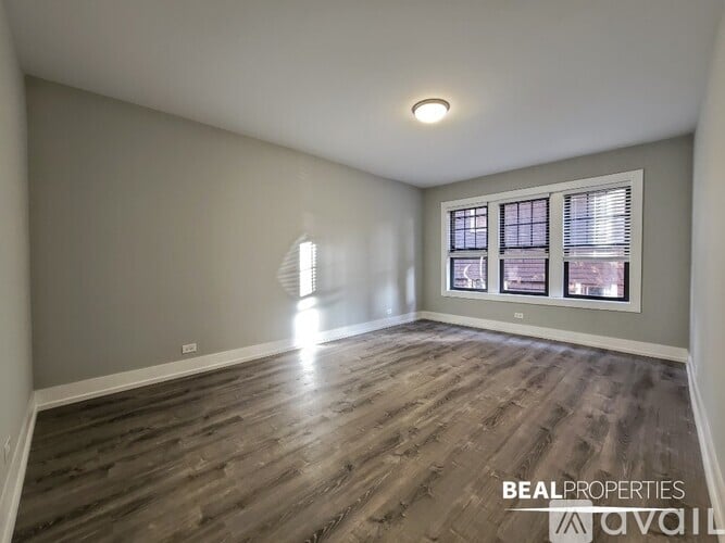 A spacious room with wooden flooring and a window with blinds.