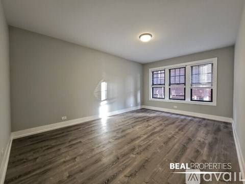 A spacious room with wooden flooring and a window with blinds.
