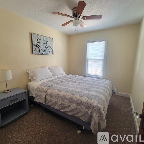 A bedroom with a bed, nightstand, and a painting of a bicycle on the wall.