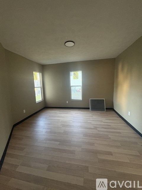 A room with wooden flooring and two windows.