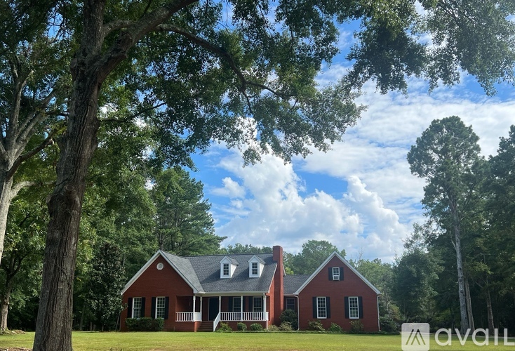 A red house with a white porch is surrounded by trees.