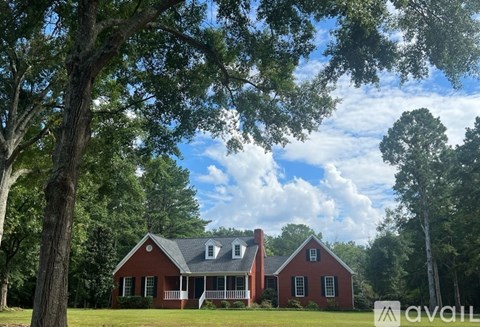 A red house with a white porch is surrounded by trees.