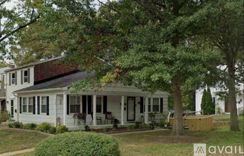 A white house with a porch and a tree in front.