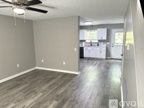 A room with a ceiling fan and a kitchen in the background.