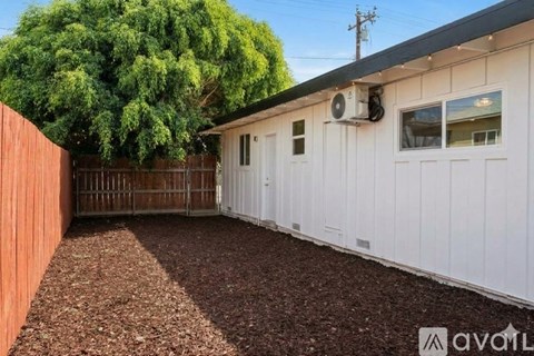 A white mobile home with a brown fence and a tree in the back.