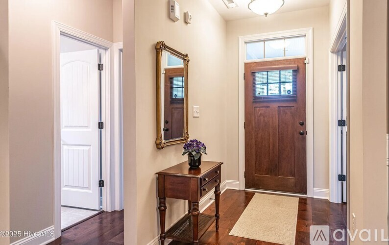 A hallway with a wooden door, a mirror, and a table with flowers on it.