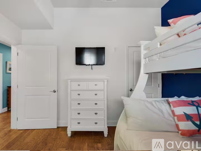 A bedroom with a white dresser and a white bed with a pillow that has an anchor on it.