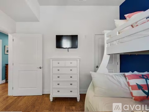 A bedroom with a white dresser and a white bed with a pillow that has an anchor on it.