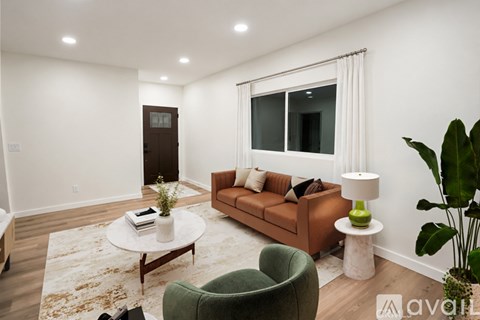 A living room with a brown couch, a green armchair, a white coffee table, and a large window with white curtains.