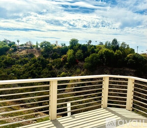 A balcony with a railing overlooks a hillside with trees and buildings.
