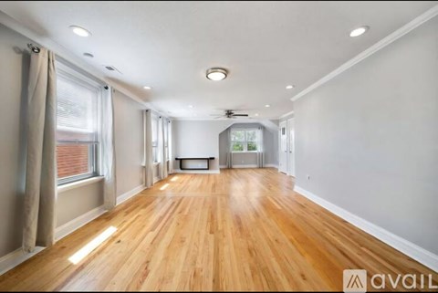 A spacious room with wooden flooring and a large window on the left side.