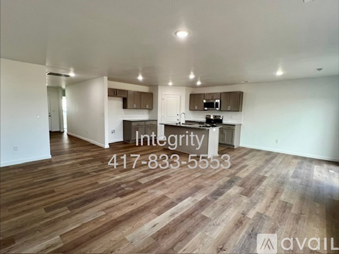 A spacious room with wooden flooring and a kitchen area in the background.