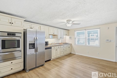 A kitchen with a refrigerator, oven, microwave, and wooden floors.