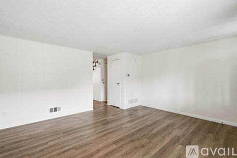 A room with wooden flooring and white walls, with a door on the right side.