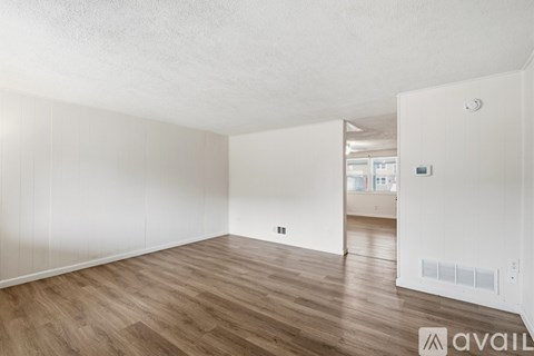 A spacious room with wooden flooring and white walls.