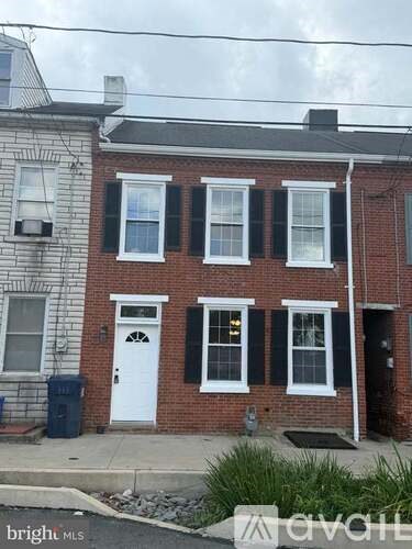 A two-story brick house with a white door and black shutters.