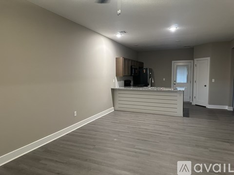 A spacious room with a kitchenette and a door leading to another room.