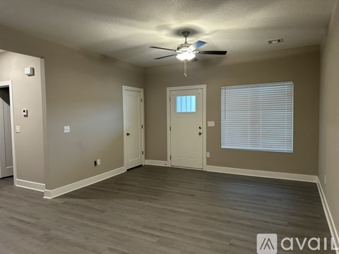 A spacious room with a ceiling fan and light, hardwood flooring, and a window with blinds.