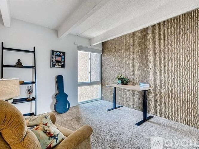 A living room with a couch, a guitar, a table, and a wall with a patterned wallpaper.