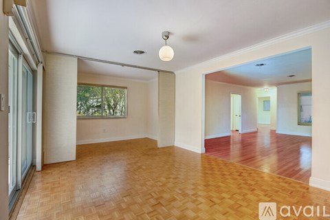 A spacious room with wooden flooring and a large window.