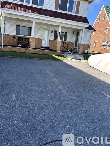 A white house with a brown fence and a driveway in front.