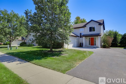 A house with a red door is surrounded by greenery and has a driveway leading to the front door.