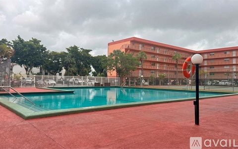 A pool with a red floor and a red building in the background.