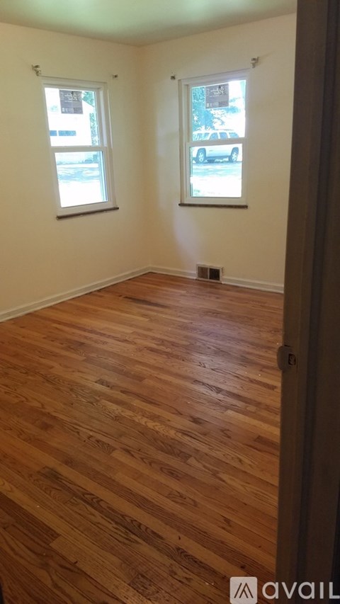 A room with wooden flooring and two windows.