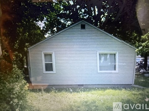 A small house with a grey siding is surrounded by trees.