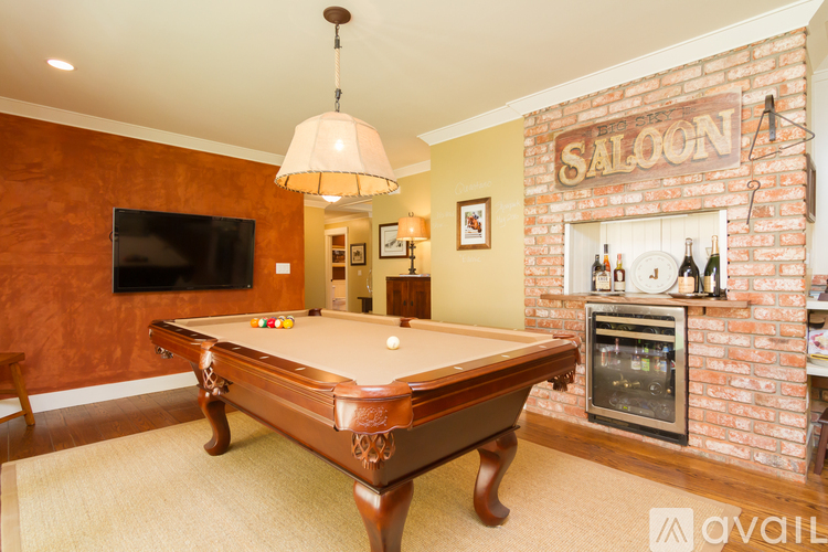 A pool table in a room with a brick fireplace and a TV mounted on the wall.